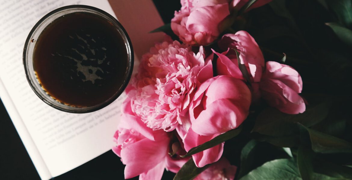 Pink peonies are are lying next to the coffee cup