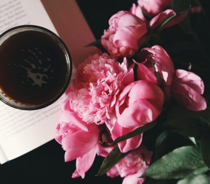 Pink peonies are are lying next to the coffee cup