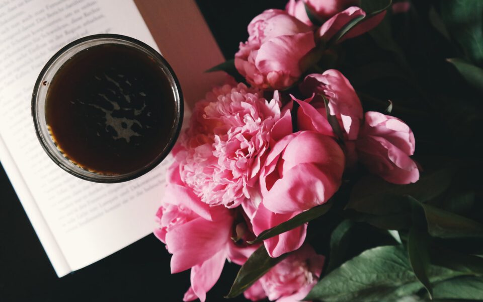 Pink peonies are are lying next to the coffee cup